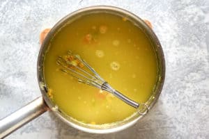 Chicken broth is being whisked into the roux in a saucepan, creating the smooth, liquid base for the Dixie Stampede soup.