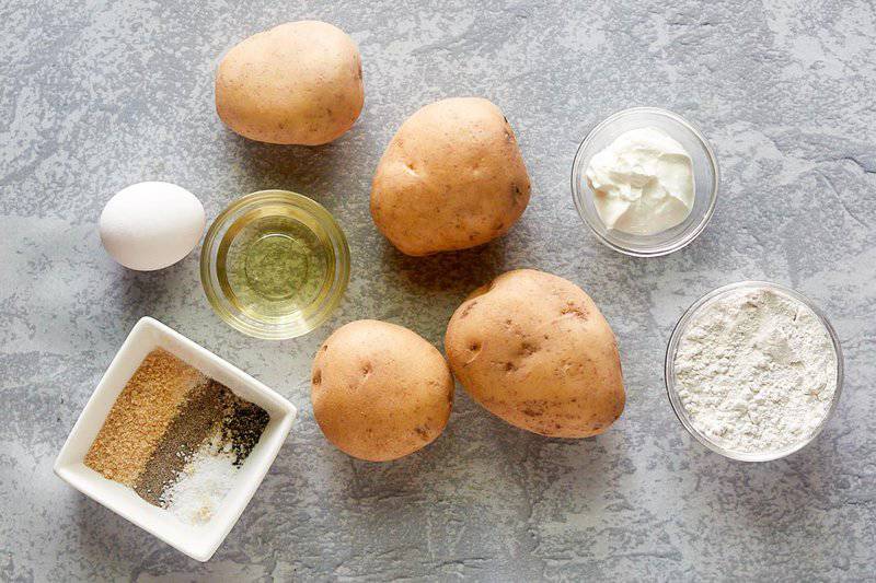 an overhead view of ingredients for mojo potatoes: raw potatoes, flour, egg, and various spices in bowls.