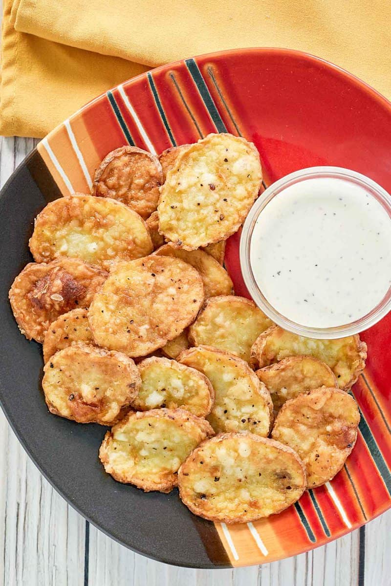 An overhead shot of a plate of crispy mojo potatoes, served with a small bowl of white dipping sauce in the center.