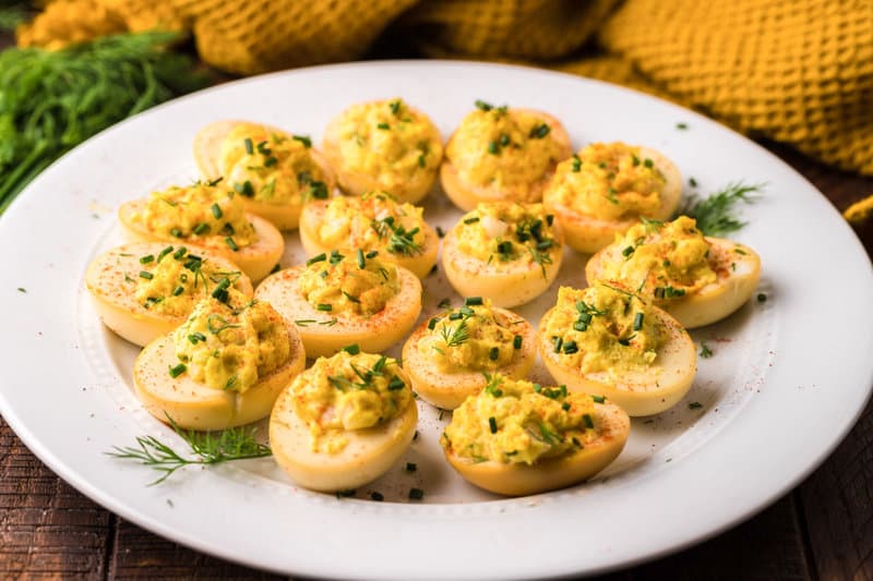 A detailed macro shot of a single smoked deviled egg. The image showcases the creamy texture of the filling, the golden color of the smoked egg white, and the fresh herb garnish.