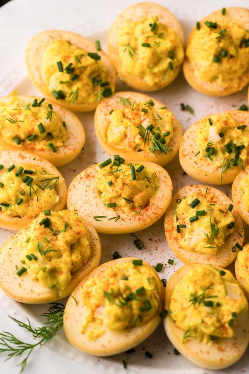 A close-up, overhead shot of a platter of smoked deviled eggs. The image focuses on the golden color of the smoked egg whites and the fresh herb and paprika garnish on the creamy filling.