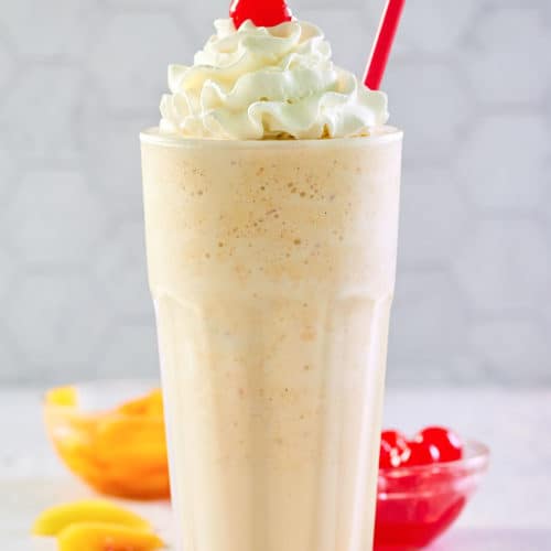 copycat Chick Fil A peach milkshake with whipped cream and a cherry.