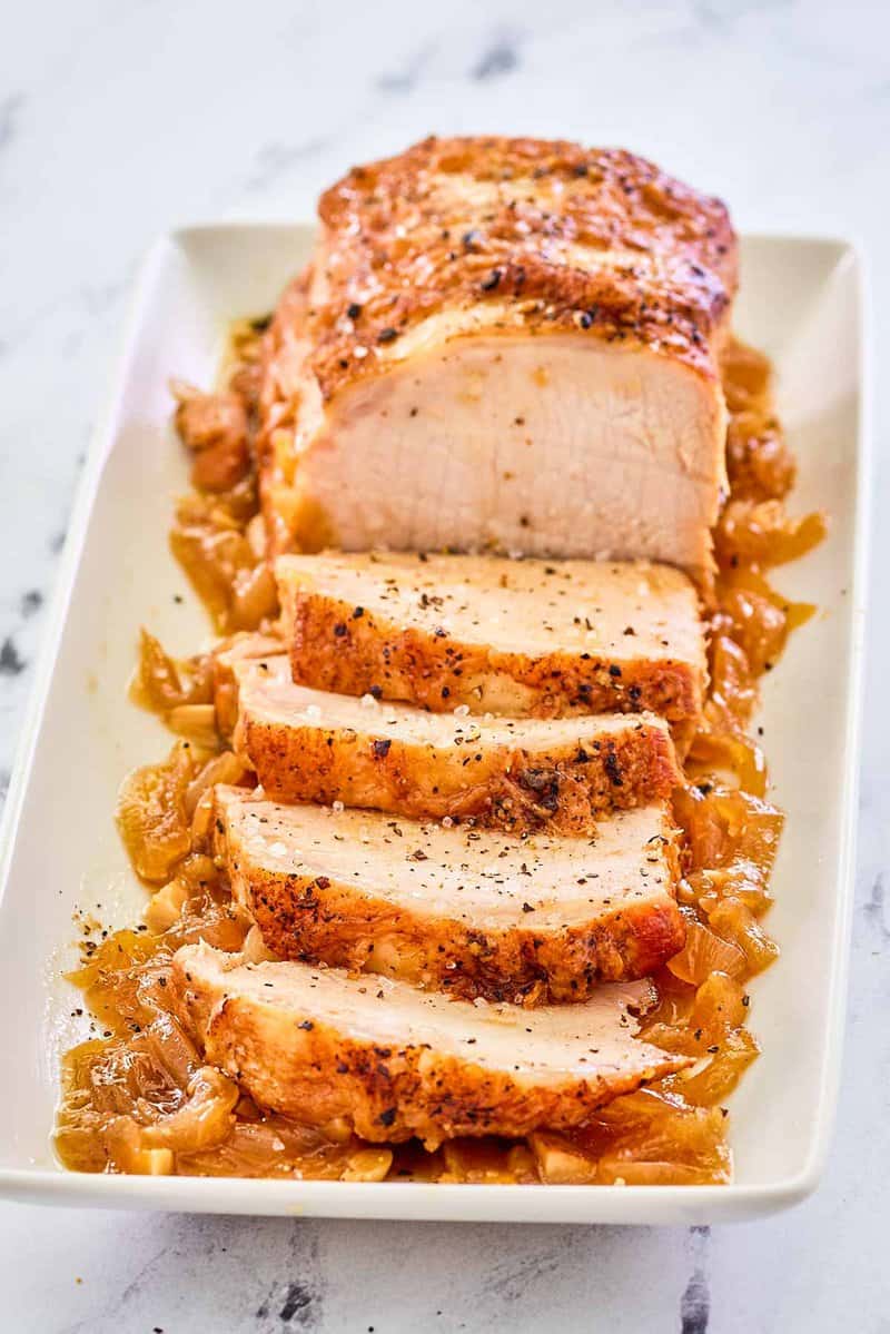 Instant Pot pork loin on top of cooked onions on a platter.