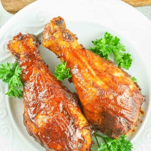 overhead view of two smoked chicken drumsticks on a plate.