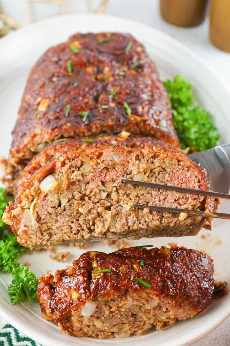 a slice of smoked meatloaf held over the meatloaf on a platter.