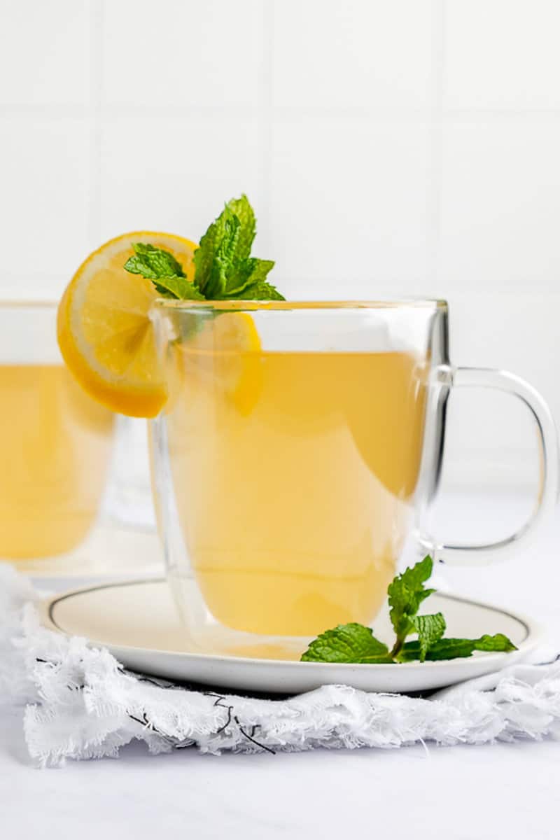 A detailed close-up of a mug of Starbucks Medicine Ball tea, focusing on the fresh garnish of a lemon slice and a sprig of mint on the rim of the glass.