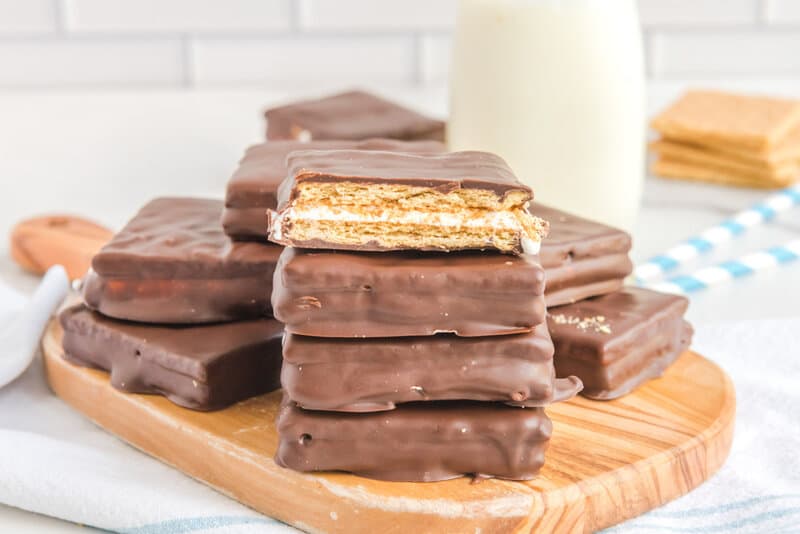 A stack of homemade chocolate S'mores cookies on a wooden board next to a glass of milk.