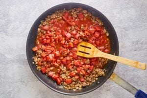 browned ground beef, onions, and tomatoes in a skillet.