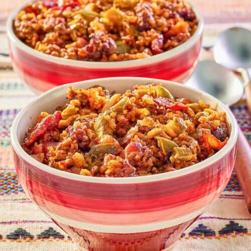 two bowls of Mexican rice casserole and spoons next to them.