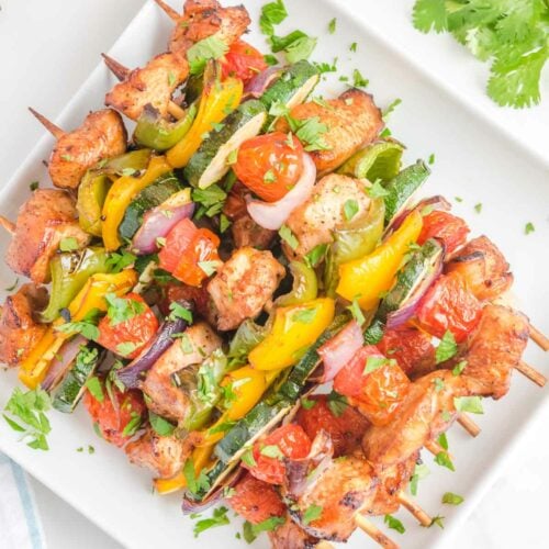 Overhead view of air fryer chicken kabobs on a square white platter.