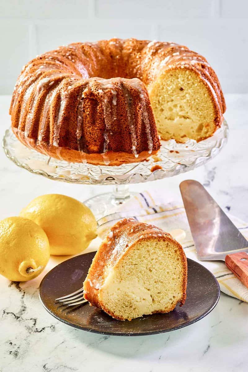 Cream cheese coffee cake on a cake stand and a slice on a plate.