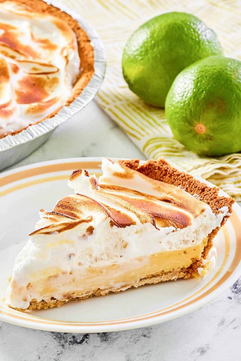 Key lime meringue pie slice on a plate and two limes.