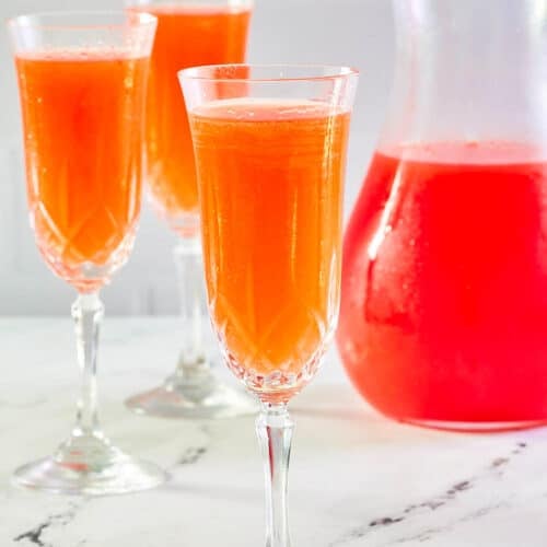 Strawberry mimosa in three glasses and a pitcher.