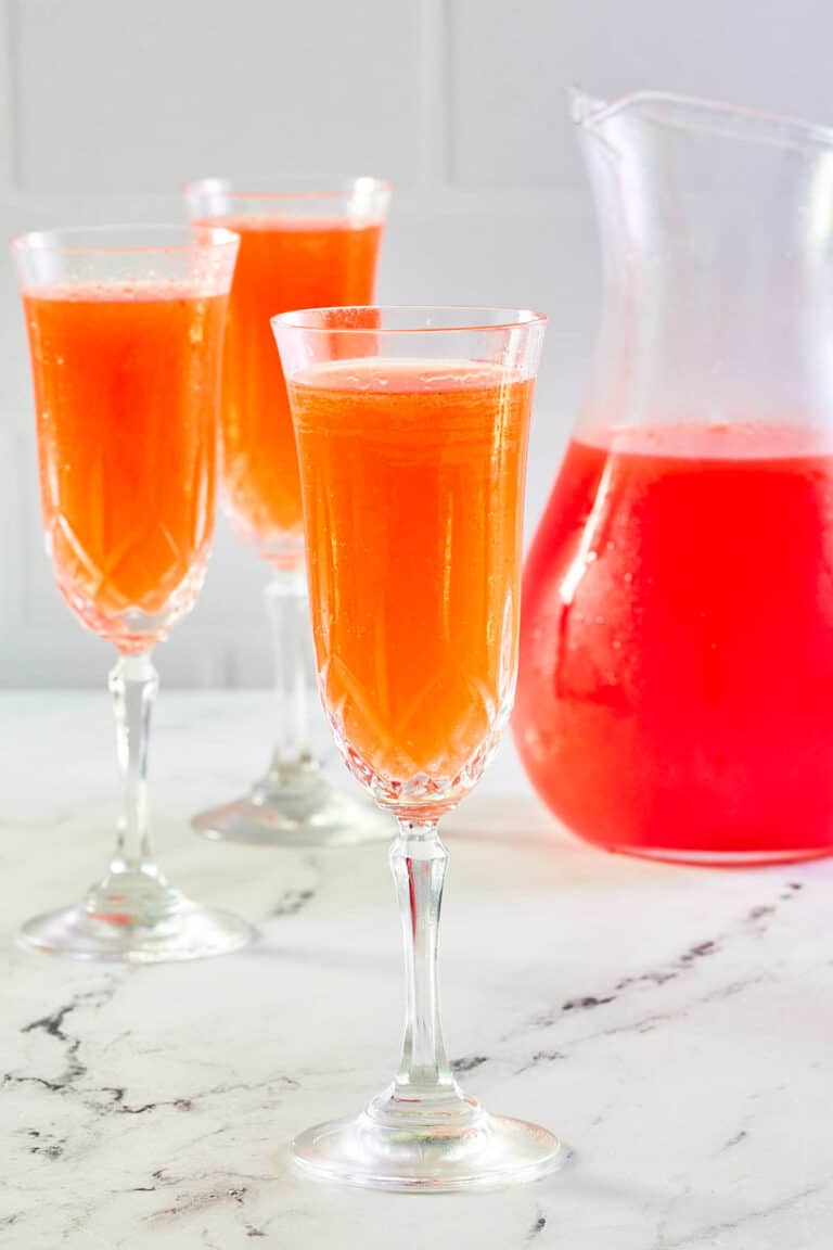 Strawberry mimosa in three glasses and a pitcher.