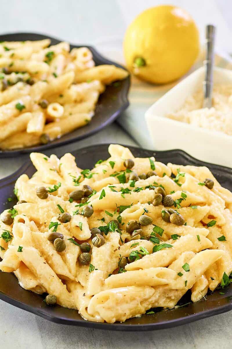 Greek pasta with lemon alfredo sauce on two plates, parmesan cheese, and a lemon.