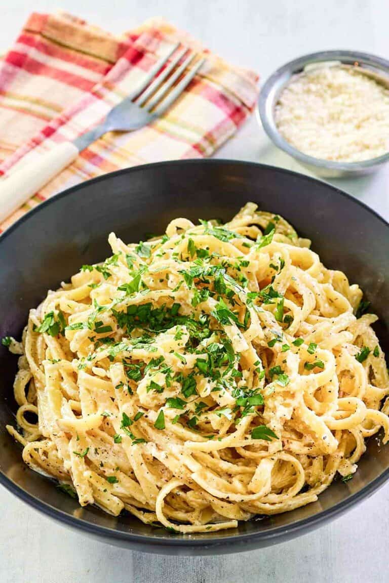 Copycat Pasta House fettuccine alfredo in a large bowl and parmesan cheese in a small bowl.