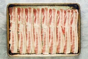 Raw bacon strips on a baking sheet.