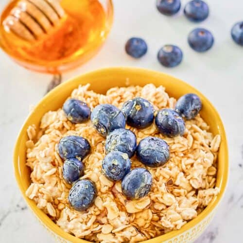 Overnight oats made with milk in a bowl, fresh blueberries, and a bowl of honey.