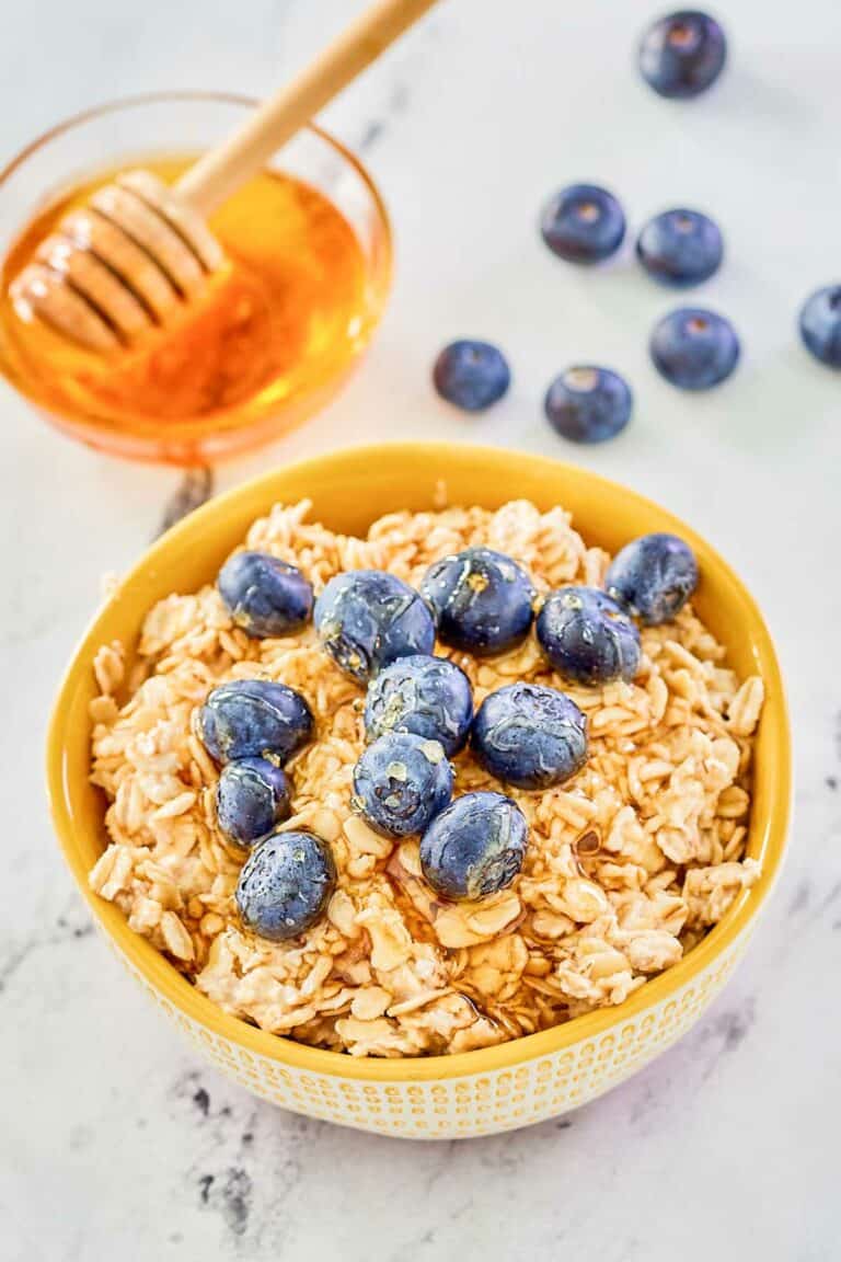 Overnight oats made with milk in a bowl, fresh blueberries, and a bowl of honey.