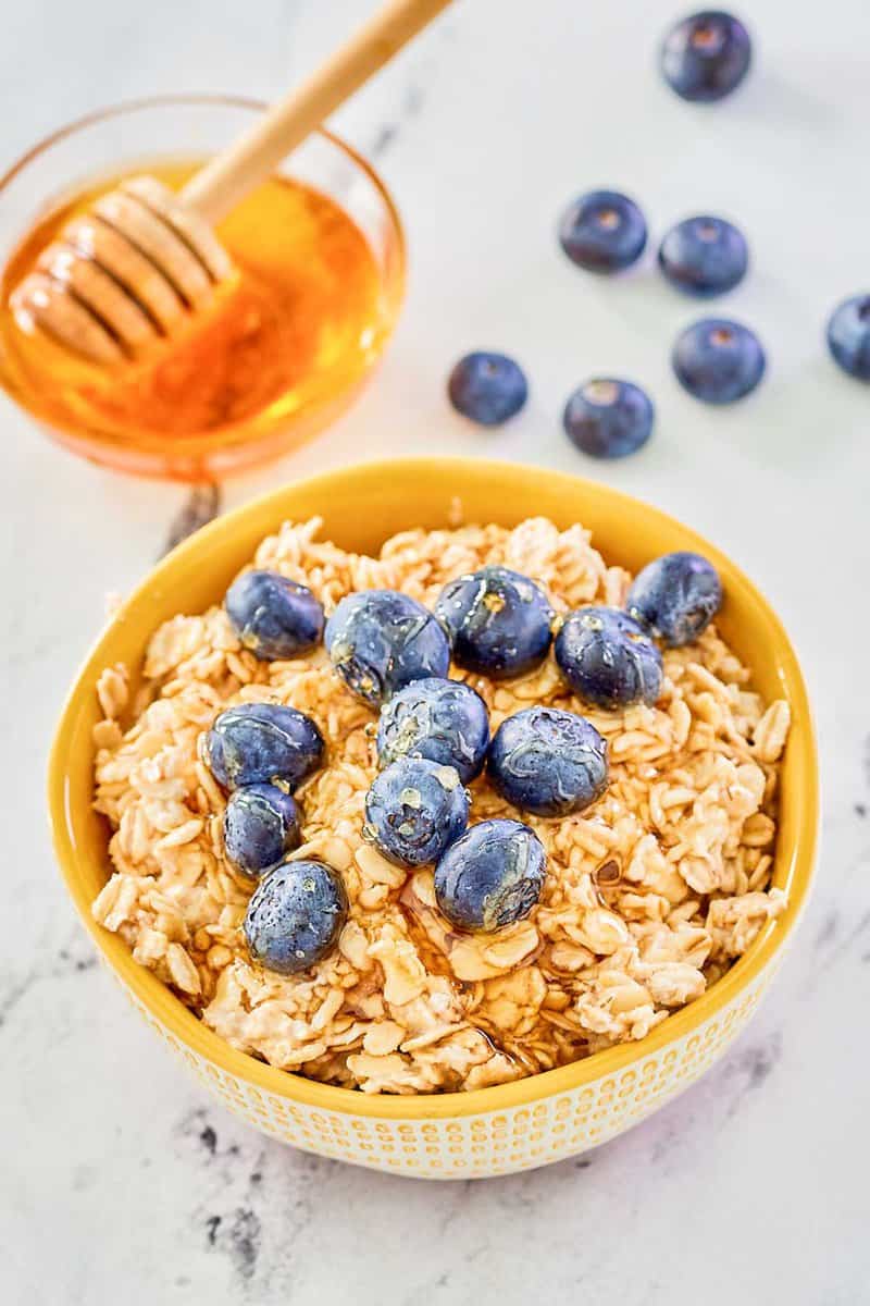 Overnight oats made with milk in a bowl, fresh blueberries, and a bowl of honey.