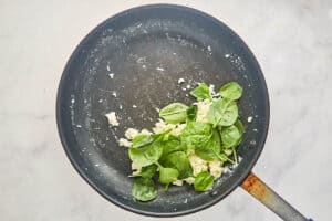 A top-down view of a skillet showing cooked egg whites with fresh spinach being added and wilted to create the filling for the wrap.