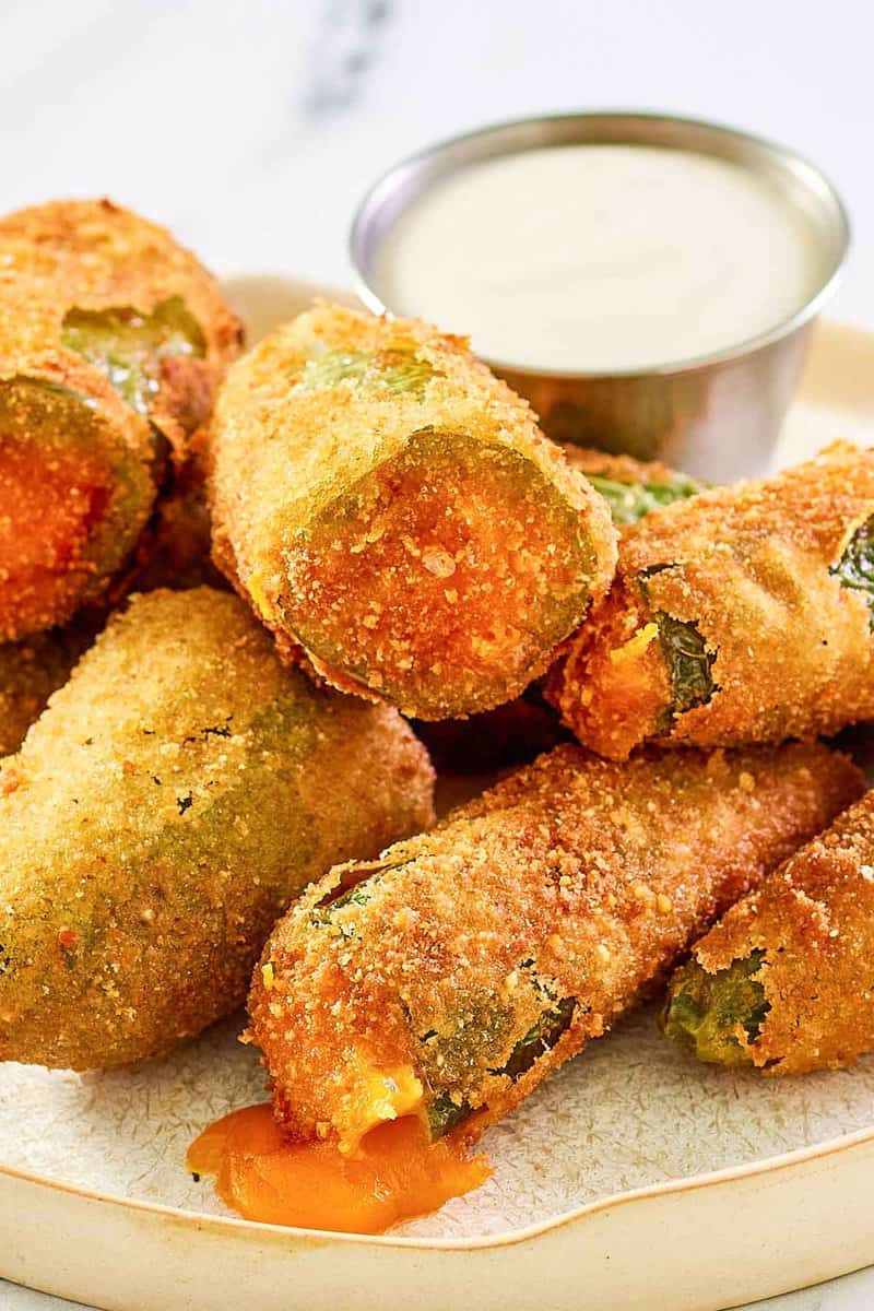 Cheddar cheese jalapeno poppers and a cup of dipping sauce on a plate.