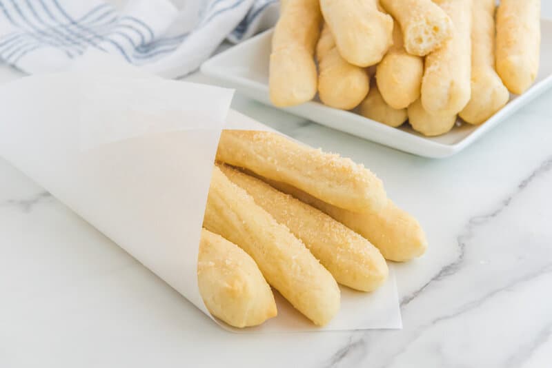 Close up of garlic butter breadsticks served in a white paper cone for a takeout look.