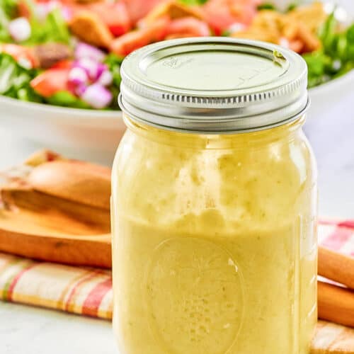 Green onion salad dressing in a mason jar and a salad behind it.