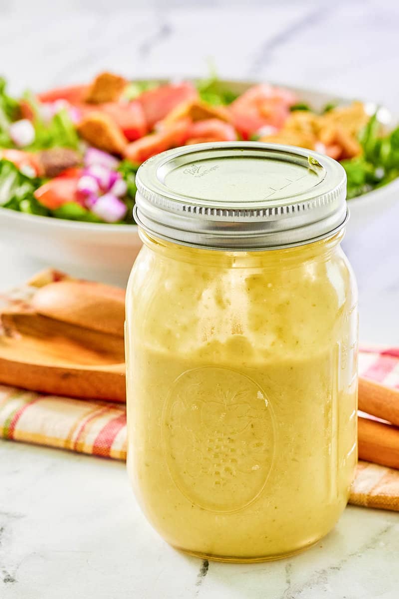 Green onion salad dressing in a mason jar and a salad behind it.