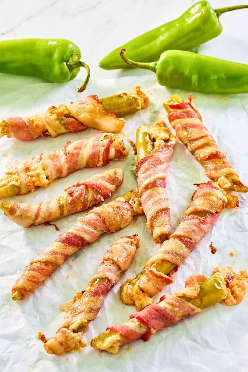 Bacon wrapped stuffed hatch peppers scattered on parchment paper.