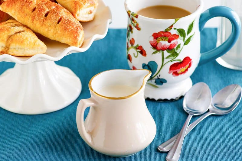 Homemade amaretto coffee creamer, cup of coffee, spoons, and pastries.