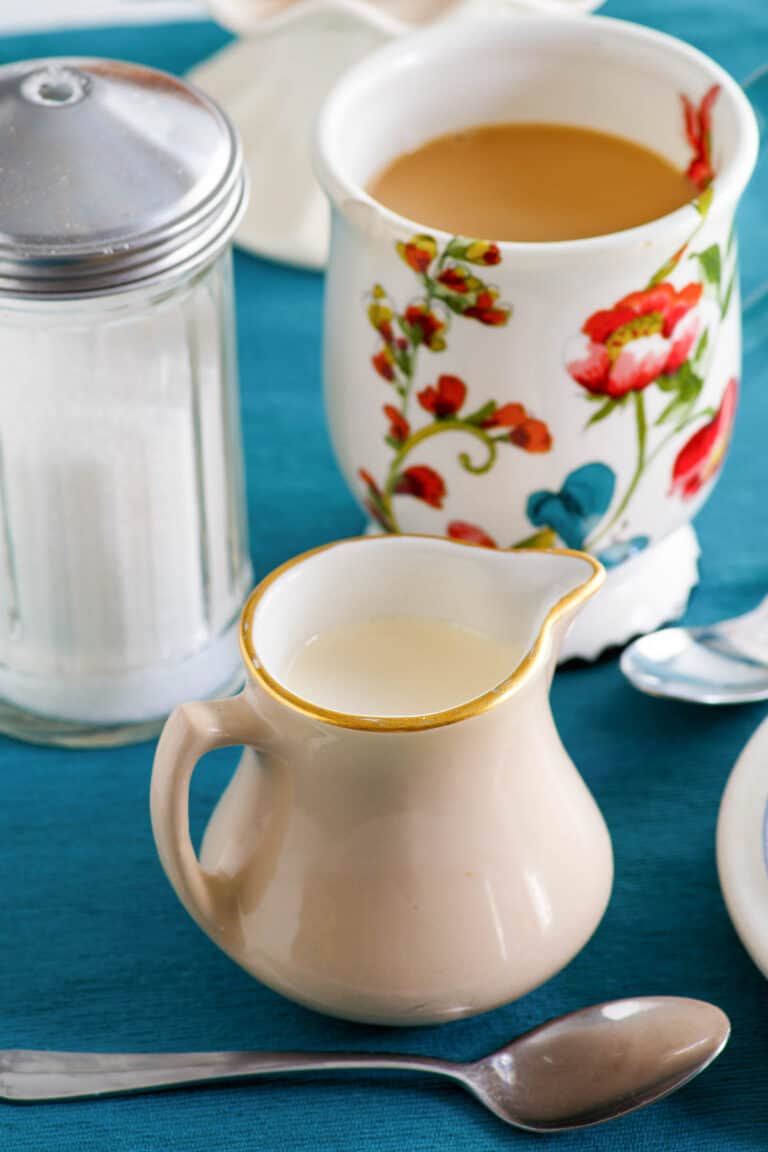 Homemade amaretto coffee creamer, a cup of coffee, and sugar.