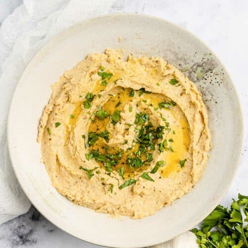 Overhead view of homemade garlic hummus, garlic bulb, lemon, and parsley.
