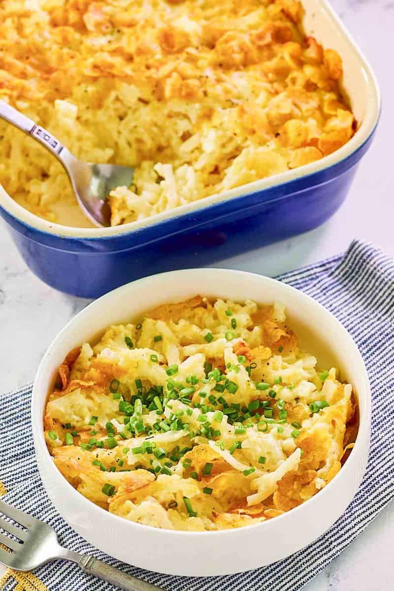Hashbrown casserole with cornflakes in a baking dish and a serving in a bowl.