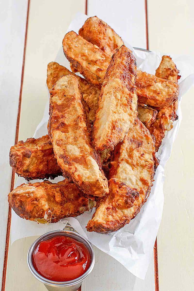 Jojo potato wedges in a serving basket and a cup of ketchup beside it.