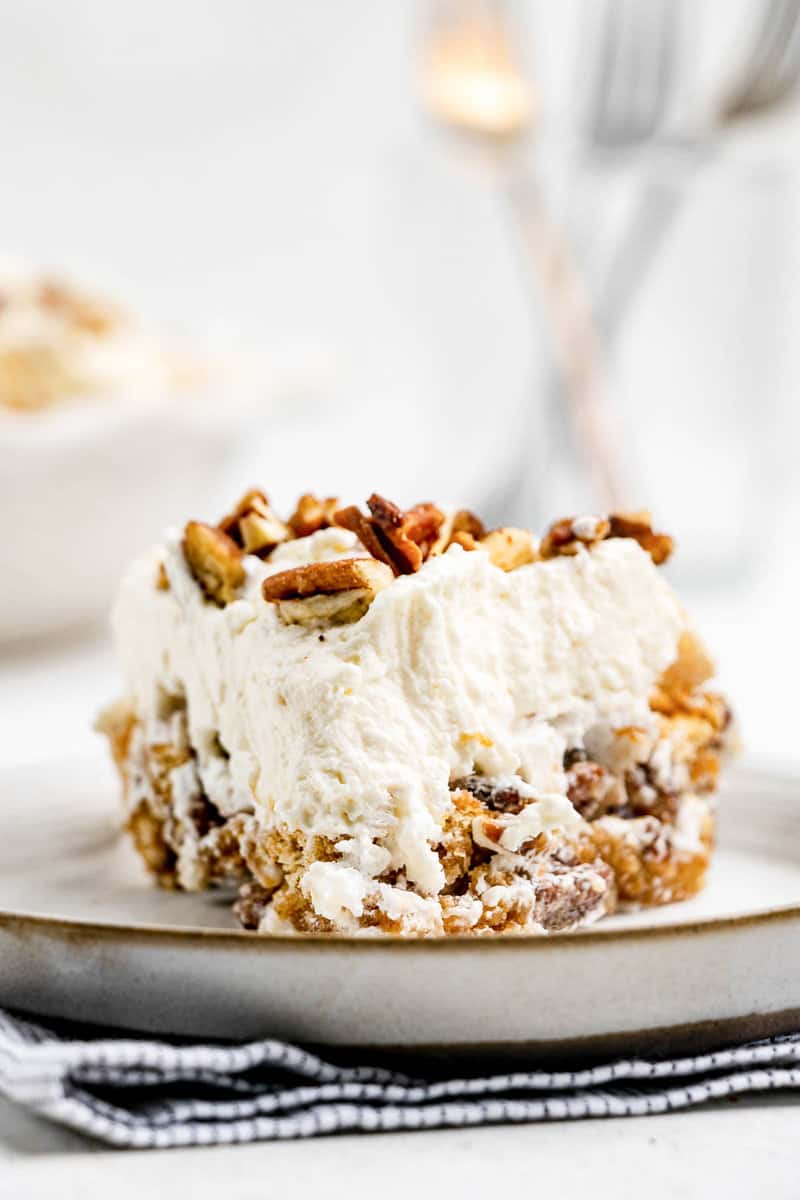 A detailed close-up of a slice of butternut brownie pie. The camera focuses on the contrasting textures of the crunchy meringue base filled with pecans and the smooth, fluffy whipped cream topping.