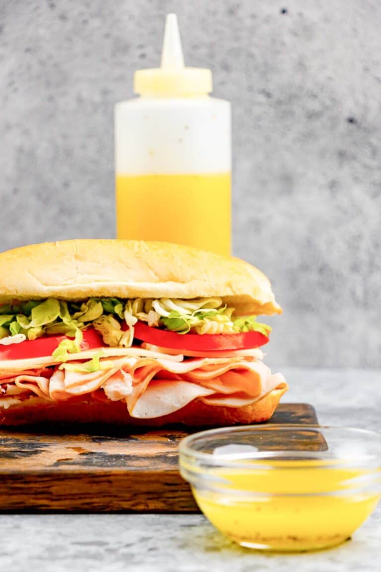 Copycat Mr. Submarine sub sauce in a small bowl and squeeze bottle and a sub sandwich.