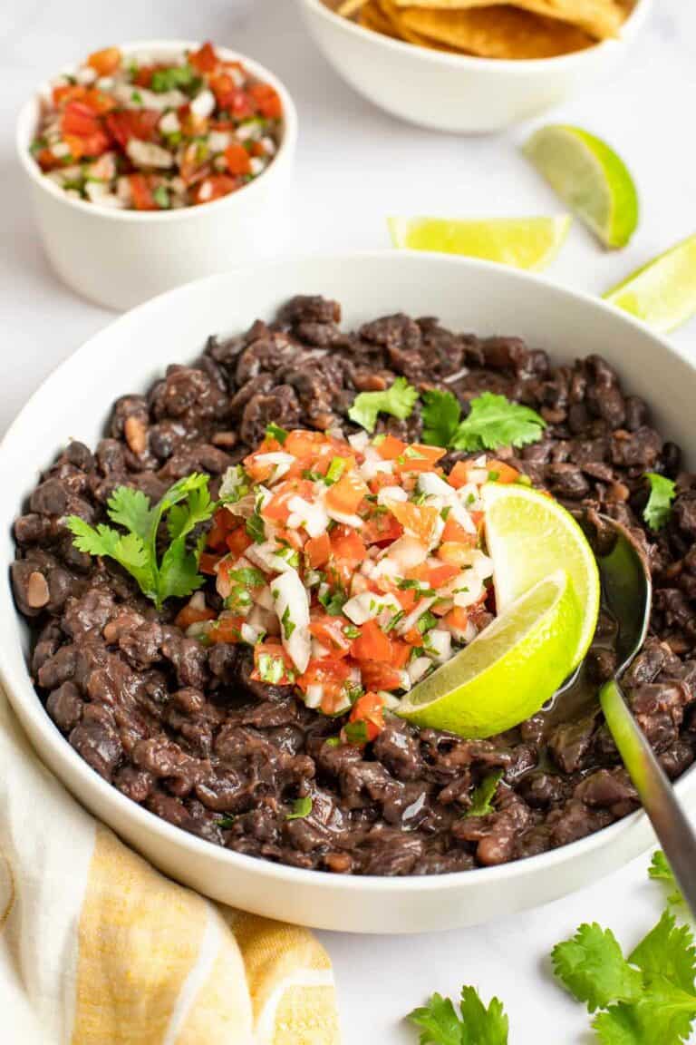 Copycat Chili's black beans garnished with pice de gallo and lime wedges.