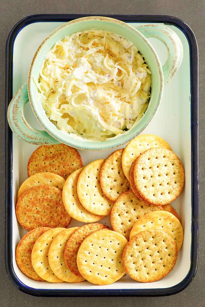 An overhead, flat-lay view of a serving tray featuring a bowl of creamy Jarlsberg cheese dip and a variety of round crackers. The appetizer is artfully arranged and ready for a party.