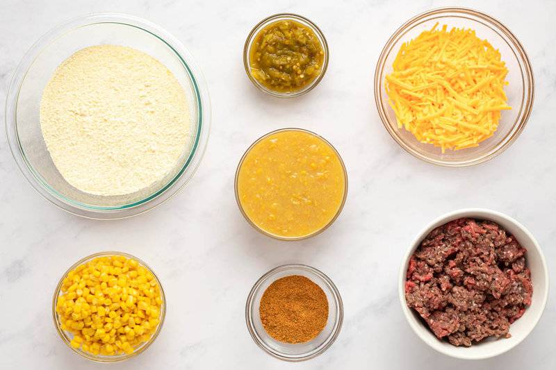 Ingredients including ground beef, corn, cheese, and cornbread mix in bowls on a counter.