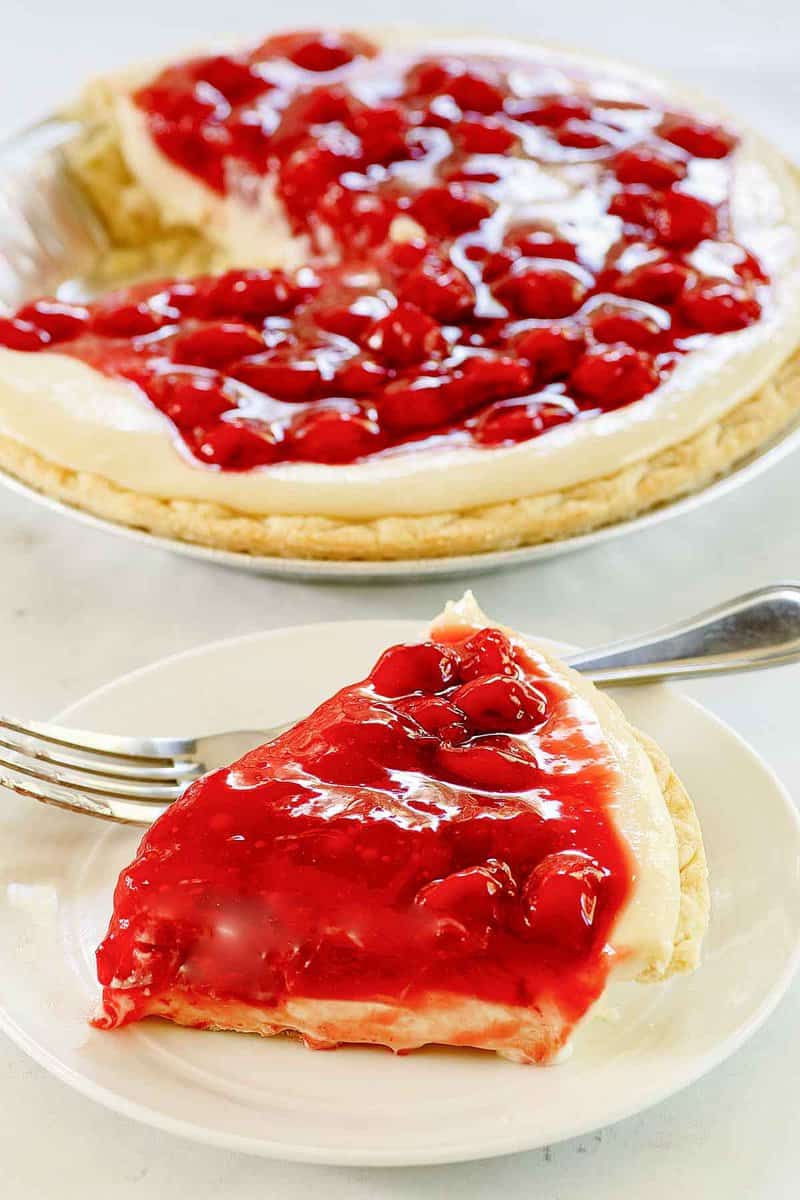 Slice of cherry cream cheese pie on a plate and the pie behind it.