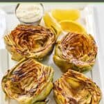 Four grilled artichoke halves, garlic aioli, and lemon wedges on a platter.