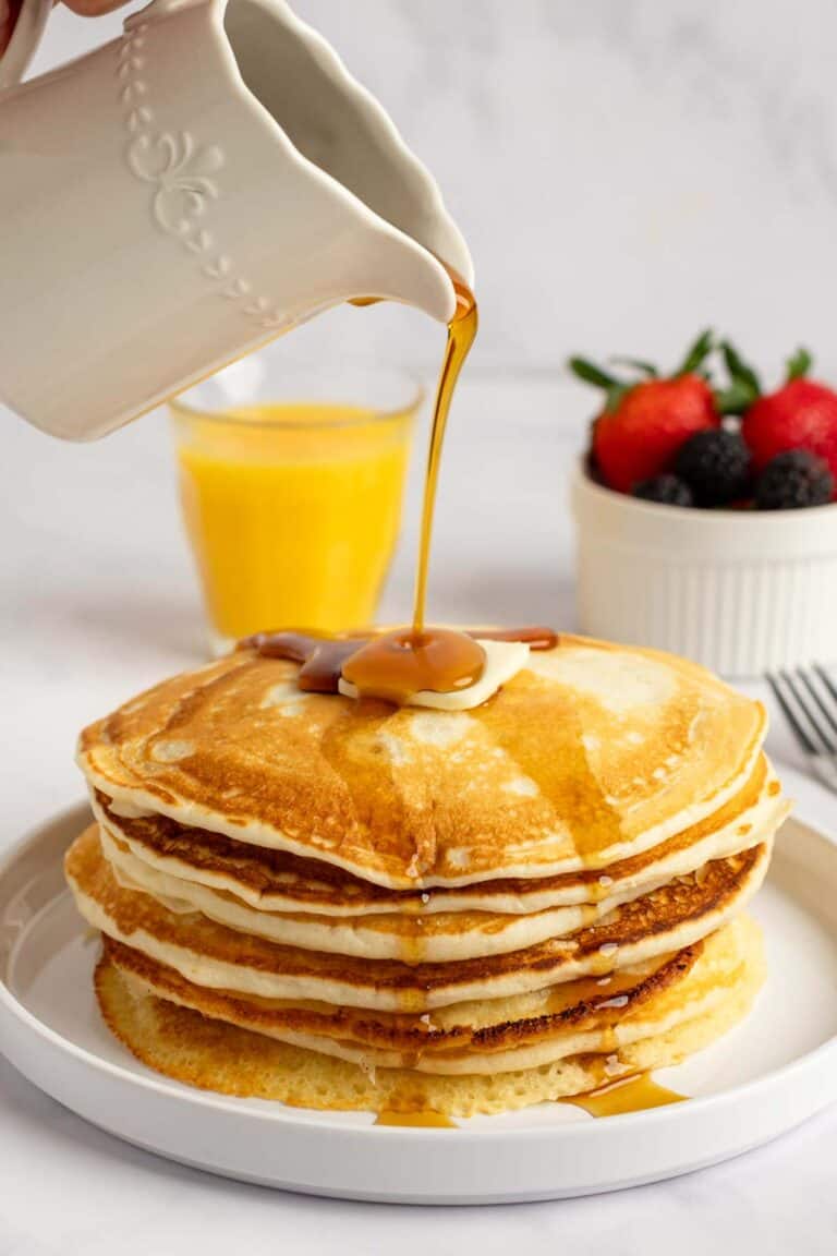 Pouring syrup over copycat IHOP buttermilk pancakes on a plate.