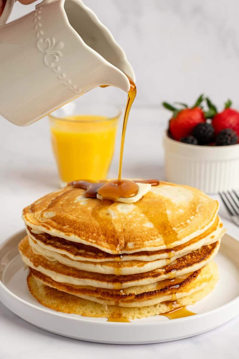 Pouring syrup over copycat IHOP buttermilk pancakes on a plate.