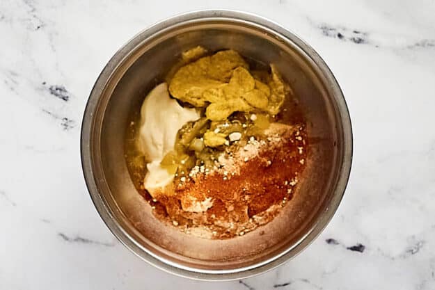 An overhead view of a stainless steel mixing bowl containing all the unmixed ingredients for the homemade Big Mac sauce. Mayonnaise, mustard, relish, and various spices are visible, ready to be stirred together.