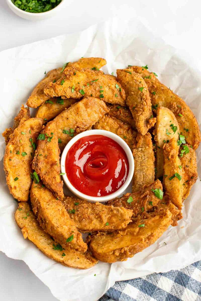 Copycat KFC potato wedges and ketchup in a serving bowl lined with parchment.