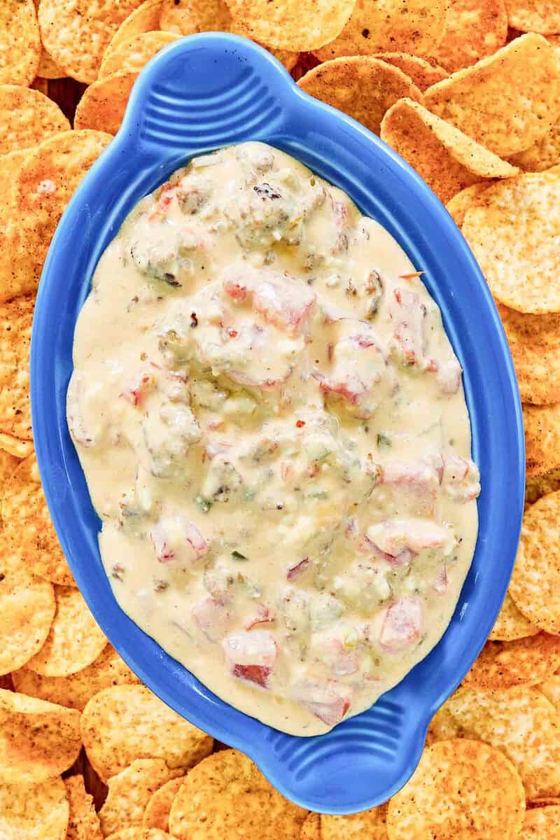 An angled close-up of a vibrant blue serving dish filled with Rotel sausage cream cheese dip. The camera focuses on the chunky, cheesy texture of the dip, with a background completely filled by crispy tortilla chips.
