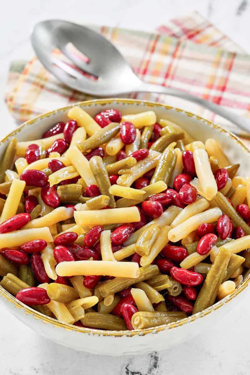 Grandma's three bean salad in a serving bowl and a slotted spoon on a napkin.