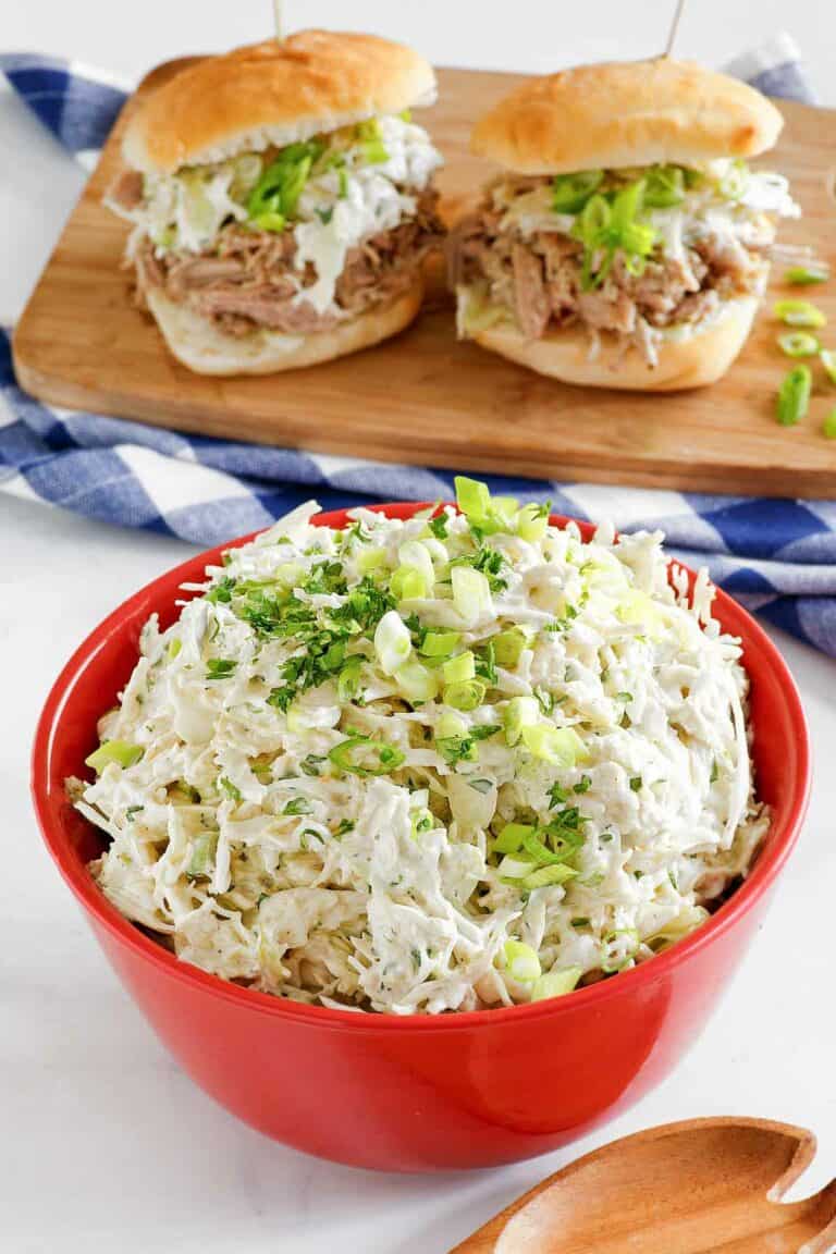 Copycat Houston's coleslaw in a bowl and two pork sliders with it on a wood board.