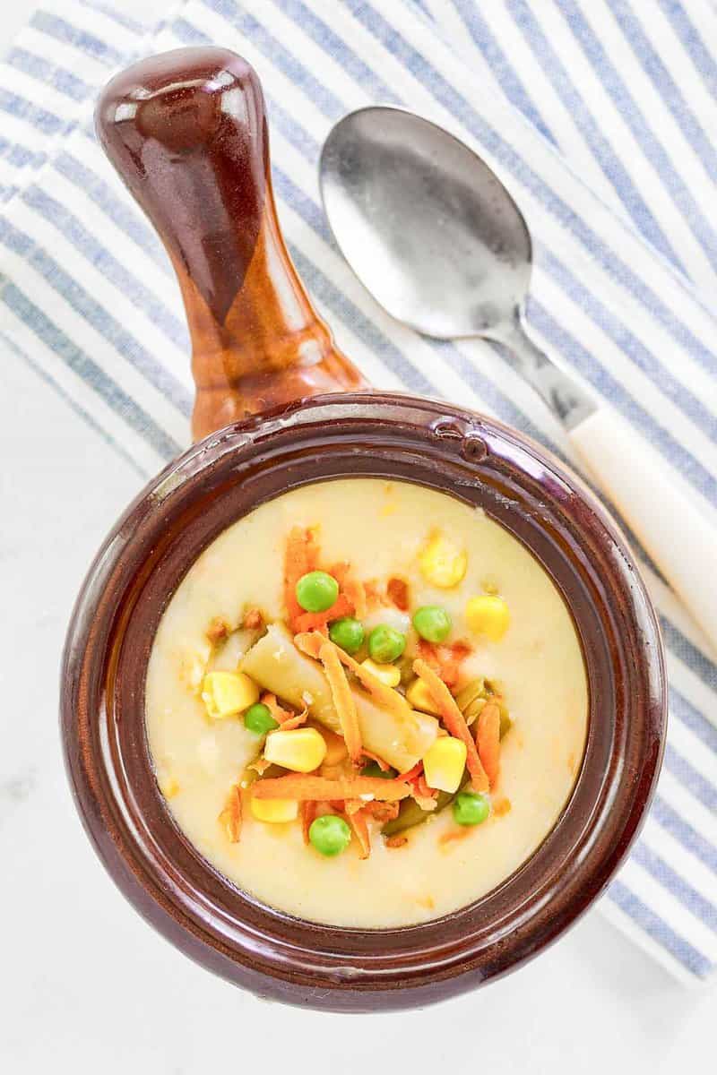 An overhead shot of Dolly Parton's Dixie Stampede soup served in a brown crock. The creamy soup is garnished with a colorful medley of vegetables.
